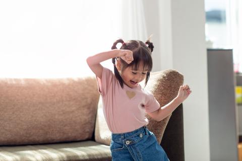 Image of young girl in pigtails dancing in front of a couch.