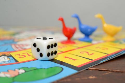 An image of various board game pieces such as a die, chickens, and a game board.