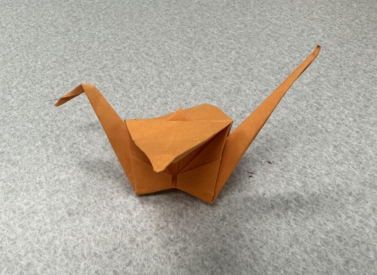 An orange origami crane is against a gray background.