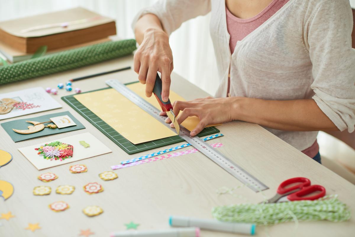 Person creating cards on a desk cluttered by crafting supplies