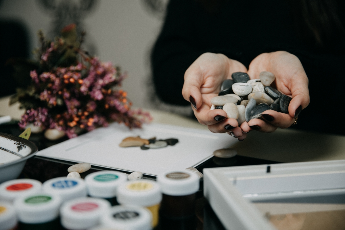Person holding pile of rocks in hand over desk full of paint supplies